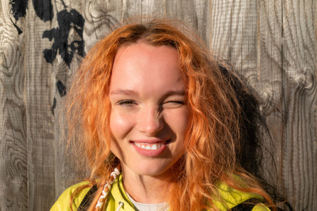 Portrait of a happy smiling young red-haired girl on the background of a wooden fence.