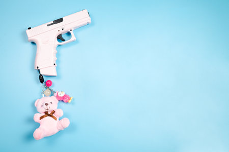 Pink automatic 9mm glock pistol with a bear and decorations on a pendant on a blue background.の写真素材
