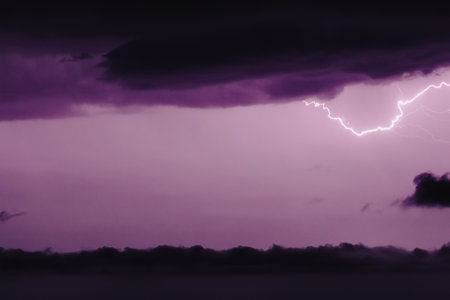 Purple or blue horizontal lightning in the night sky in black clouds. A real photo of a thunderstorm. The concept of meteorology.の写真素材