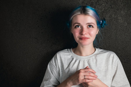 Portrait of a confusion woman in a white T-shirt with blue hair on a dark backgroundの写真素材