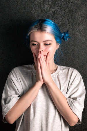 Portrait of a confusion woman in a white T-shirt with blue hair on a dark background