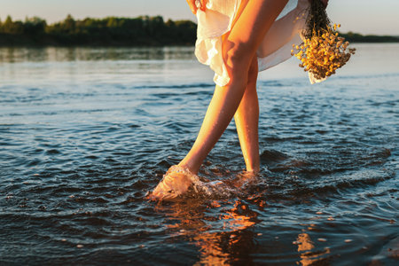 Barefoot girl in a white dress walks on the water with a dry bouquet of flowers against the background of the sunset sky. The concept of pagan ritual.の写真素材