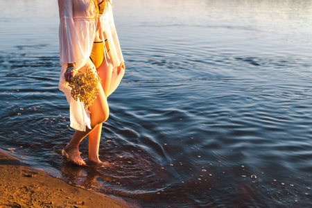 Barefoot girl in a white dress walks on the water with a dry bouquet of flowers against the...