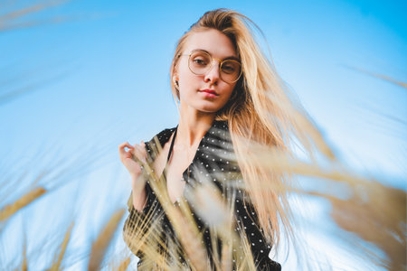 A beautiful and sensual blonde woman in a black dress with white polka dot stands in a field of...