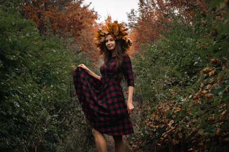 Brunette woman in a wreath of maple leaves in a dress on the background of an autumn park or forest.