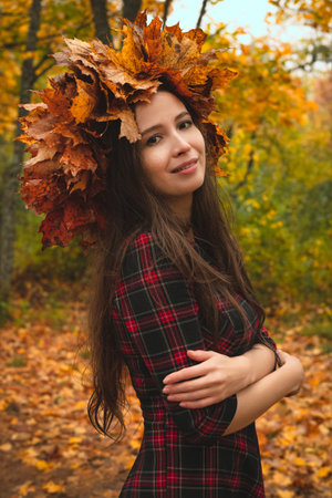 Brunette woman in a wreath of maple leaves in a dress on the background of an autumn park or forest.の写真素材