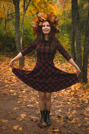 Brunette woman in a wreath of maple leaves in a dress on the background of an autumn park or forest.の写真素材