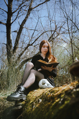 Woman sitting in a black robe with a skull and book in the dark forest swamp. Mystical portrait of a witch. The concept of witchcraft and occultism.の写真素材