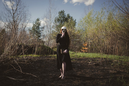 Woman dance in a black robe with a skull and book on burnt grass. A mystical portrait of a witch. The concept of witchcraft and occultism.の写真素材