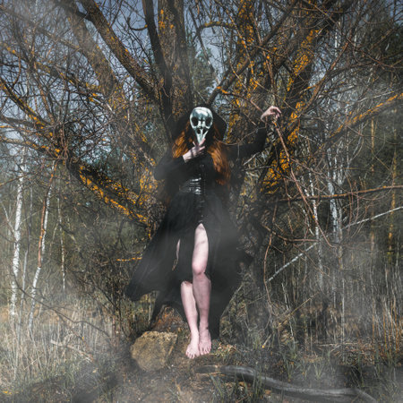 Woman in a black robe with a skull and a book in a dark forest. A mystical portrait of a witch. The concept of witchcraft and occultism.の写真素材