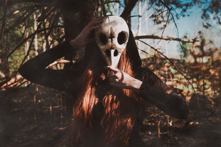 Woman in a black robe with a skull and a book in a dark forest. A mystical portrait of a witch. The concept of witchcraft and occultism.の写真素材