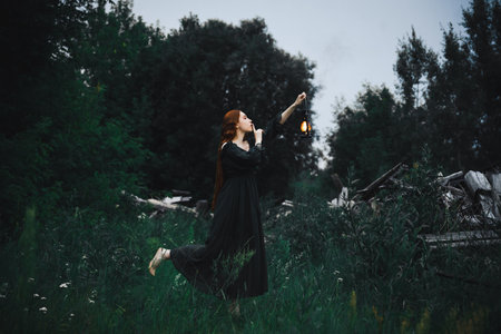 Lonely woman in a black dress with a kerosene lamp in her hands walks through the night forest near the ruins. The concept of fairy tale mysticism.の写真素材