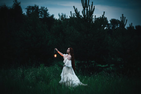 Lonely woman in a white dress with a kerosene lamp in her hands walks through the night field. The concept of fairy tale mysticism.の写真素材