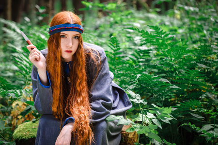 A young woman in a medieval Slavic or Nordic traditional costume. A robber girl with a knife in the forest.の写真素材
