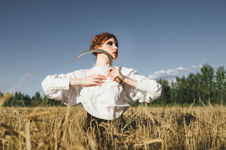 Slavic girl in a white dress and a black skirt with witch makeup stands in a field of rye and holds...