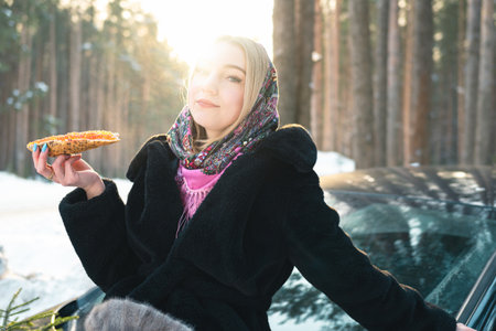Portrait woman in a black fur coat, which sits on the hood of a car and eat caviar with bread.の写真素材