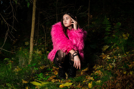 An eccentric young woman poses in a pink fur coat and torn tights in a dark green forest.の写真素材