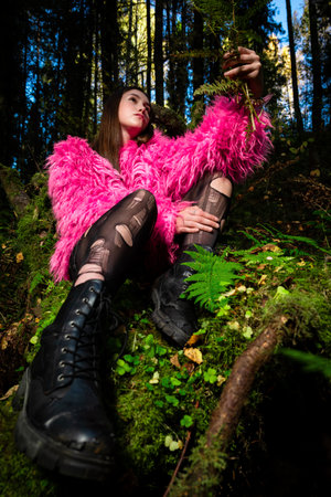 An eccentric young woman poses in a pink fur coat and torn tights in a dark green moss forest.の写真素材