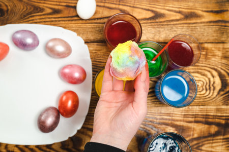 Woman paints Easter eggs on a wooden table with dyes, a close-up photo of her hands. The concept of a happy Easter.の写真素材