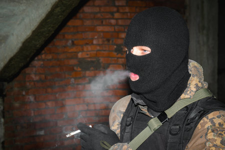 Portrait of a military smoking cigarette man with blue eyes in a black balaclava and camouflage.の写真素材