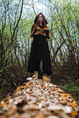 Gothic red haired woman in a black long dress in a gloomy forest. Mystical witch girl.