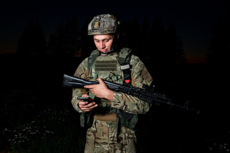 Portrait of a military man in camouflage clothing with an assault rifle on the background of a night...