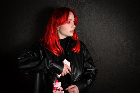 Portrait of a young woman with red hair on a black background. A girl in black leather clothes holds a pink pistol in her hand. The concept of self-defense or self-protection.の写真素材