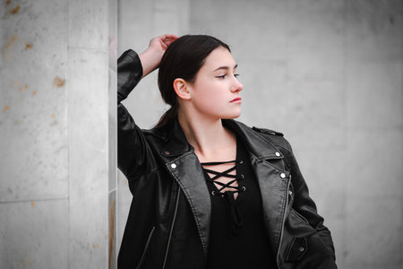 Portrait of a black haired young girl in black clothes and a leather jacket posing thoughtfully...
