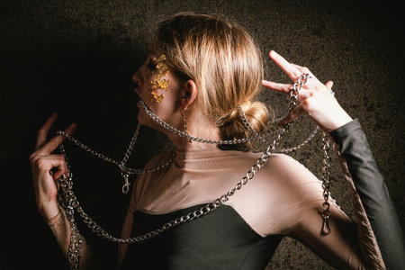 Portrait of a drunken woman in chains with a gold make-up on a dark background. Tipsy girl is trying to free herself from chains. Concept of psychology.の写真素材