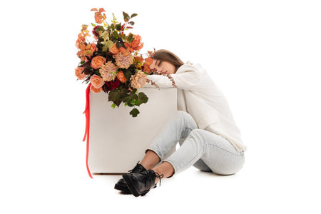 Woman in a white jacket is sitting on the floor with a bouquet of roses. Studio photo on a white background.の写真素材