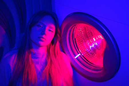 Young woman in a neon lighting washing machine. Concept of cyberpunk household chores.
