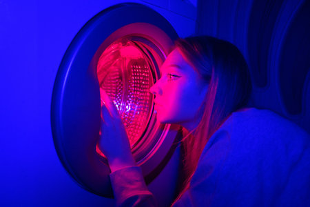Young woman in a neon lighting washing machine. Concept of cyberpunk household chores.