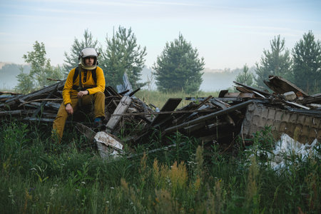 Man in an astronaut helmet is sitting on the ruins of a wooden building in the forest and is sad....