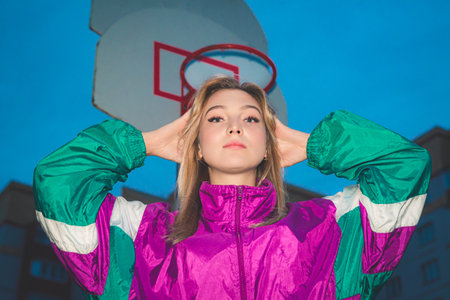 Woman wearing a vibrant retro jacket is standing on a basketball court with hands in a prayer...