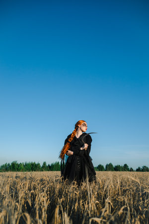 Hooded woman with a scythe stands in a field, exuding a mystical and eerie vibe, suggesting a ritual or witchcraft.の写真素材