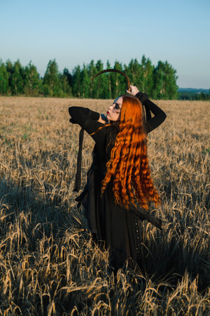 Hooded woman with a scythe stands in a field, exuding a mystical and eerie vibe, suggesting a ritual or witchcraft.の写真素材