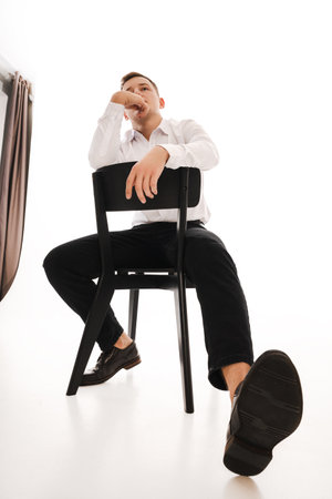 25 years man in a white shirt and blue tie sits on a chair. Concept of formal corporate photographyの写真素材