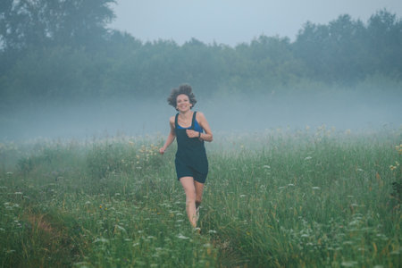 Curly haired 30 year old woman walks in the morning misty field.の写真素材