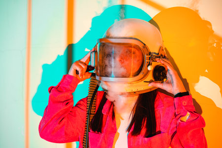 Woman in an astronaut helmet, with smoke emerging, stands against a bright orange background, evoking space exploration and mystery.の写真素材