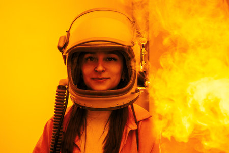 Woman in an astronaut helmet, with smoke emerging, stands against a bright orange background,...