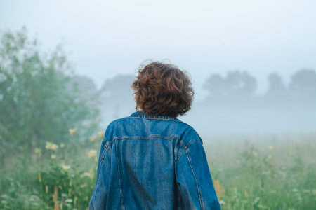 Curly haired 30 year old woman in a sundress walks in the morning misty field.の写真素材