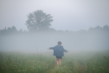 Curly haired 30 year old woman in a sundress walks in the morning misty field.の写真素材