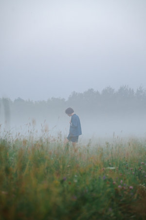 Curly haired 30 year old woman in a sundress walks in the morning misty field.の写真素材