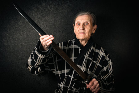 An elderly woman poses with an ancient sword in a housecoat.の写真素材