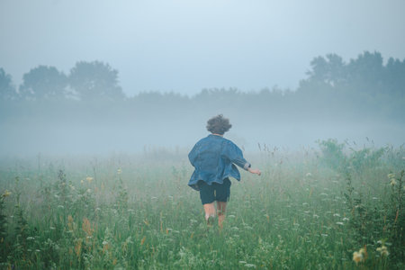 Curly haired 30 year old woman in a sundress walks in the morning misty field.の写真素材