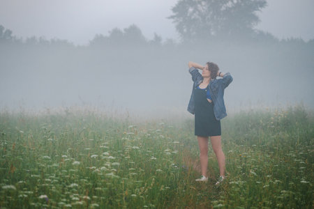 Curly haired 30 year old woman walks in the morning misty field.の写真素材