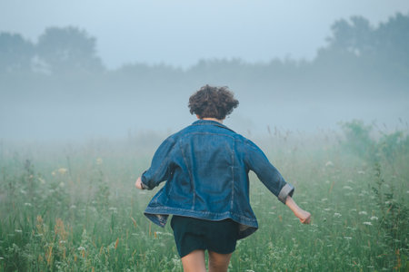 Curly haired 30 year old woman in a sundress walks in the morning misty field.の写真素材