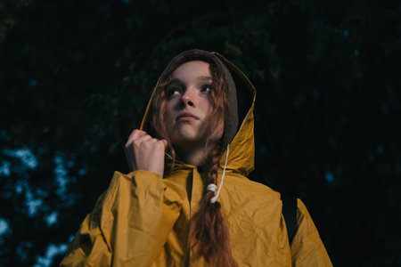 Portrait of a red haired young woman in a yellow raincoat during the rainの写真素材