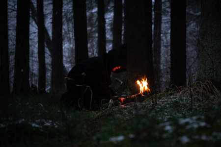 Sorcerer in cloak black and torch is conjuring in a winter forest against a background of thick smoke.の写真素材