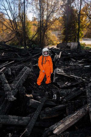 Astronaut in an orange suit on the ruins of a burnt-out building. The charred remains of a wooden house at the disaster site.の写真素材